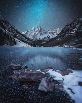 View of maroon bells reflecting in a serene lake under a starry sky, Aspen, Colorado, United States.