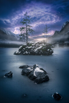 View of serene Hintersee lake surrounded by majestic snow-covered mountains and tranquil trees at twilight, Ramsau bei Berchtesgaden, Bavaria, Germany.