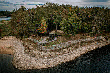 Aerial view of a secluded lakeside area with a wooden observation deck, stone embankment, and lush...