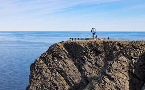 View of rugged cliffs overlooking the Barents Sea with a globe sculpture and tourists, North Cape, Finnmark, Norway.