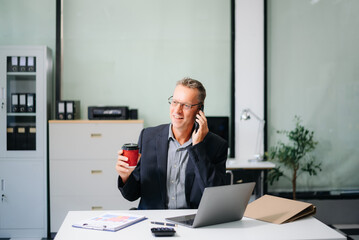Naklejka premium Confident businessman working on finance analysis with a tablet and laptop at office desk. Perfect for business