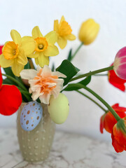 An Easter card. Colorful bright tulips decorated with eggs are in a vase on the table next to colorful eggs. Vertical photography