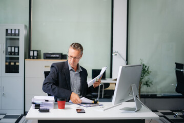 Confident businessman working on finance analysis with a tablet and laptop at office desk. Perfect for business
