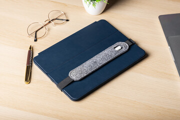 Handmade Felt gray case for stylus lies on tablet in blue case. Stylus and tablet on light wooden...