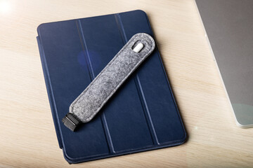 Handmade Felt gray case for stylus lies on tablet in blue case. Stylus and tablet on light wooden...