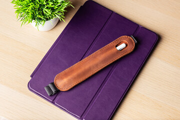 Handmade brown leather case for a stylus lies on a tablet in a purple case. Stylus and tablet on a...