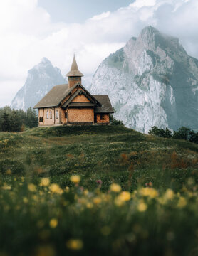 View of serene meadow with wildflowers and a charming wooden chapel surrounded by majestic mountains, Stoos, Schwyz, Switzerland.