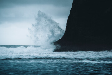 View of dramatic waves crashing on a black sand beach with rocky cliffs under an overcast sky, Playa de Benijo, Santa Cruz de Tenerife, Spain.