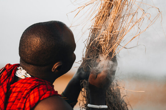 Manyara, Tanzania - 03 February 2024: View of a traditional masai person starting a fire amidst dry grass with smoke, Manyara, Arusha, Tanzania.