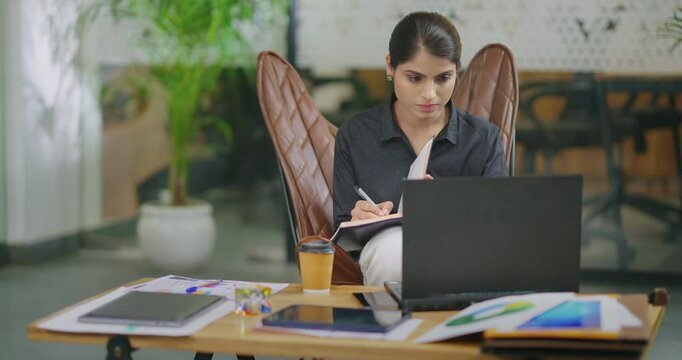 Indian gen z busy woman lady sitting chair use laptop on desk table look screen check email job office place young adult expert girl staff female do online work search day task data new idea planing