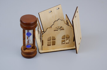 Destroyed house and hourglass on gray background. Aging process and house destruction concept.