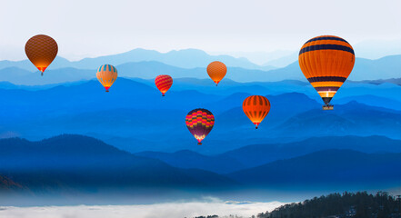 Hot air balloon flying over beautiful landscape with cascade blue mountains at the morning - View of wilderness mountains during foggy weather