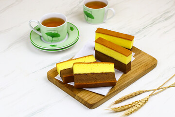 Lapis Surabaya or Indonesian layered sponge cake on wooden chopping board with cups of tea. White marble background.