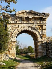 Explore an ancient stone arch in a historic site surrounded by lush greenery and clear skies during the afternoon