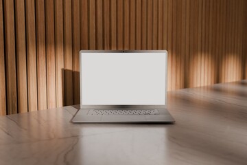 Mockup laptop computer on bamboo tabletop against acoustic panel wall in the back, hit by sunlight. 