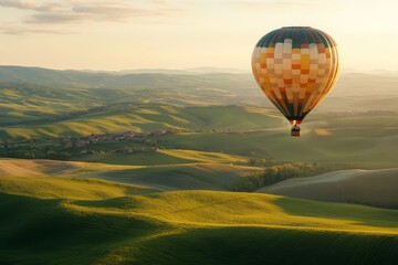 Fototapeta premium A colorful hot air balloon drifts over rolling green hills at sunrise, embodying freedom and adventure in a serene landscape.