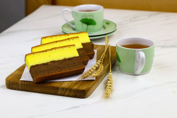 Lapis Surabaya or Indonesian layered sponge cake on wooden chopping board with cups of tea. White marble background.