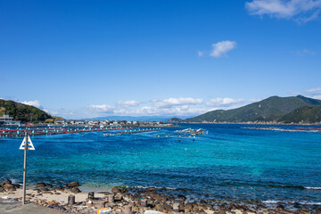 岬の見えるエメラルドグリーンの美しい海にいけすが浮かぶ海岸