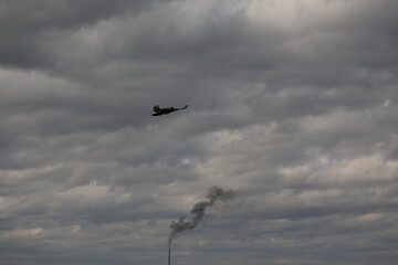A small chimney with smoke in the distance. A bird in a cloudy sky with gray clouds