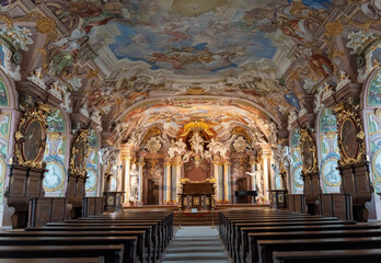 Baroque church interior with stunning frescoed ceiling, golden altar, and ornate decorations. Rows...