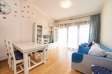 Beige living room with large sofa, table, chairs and wardrobe with TV