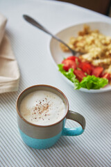 Breakfast table. Cup of coffee and plate with scrambled eggs and vegetables on the table
