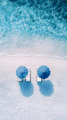 top down view of two blue umbrellas and beach chairs on white sand by clear turquoise water
