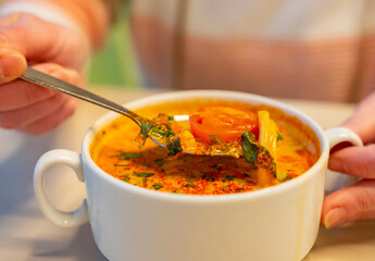 Man eats tom yum soup, showing ingredients of dish on spoon in close-up.