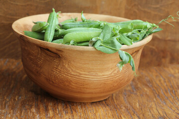 Green pea pods in wooden bowl on rustic background
