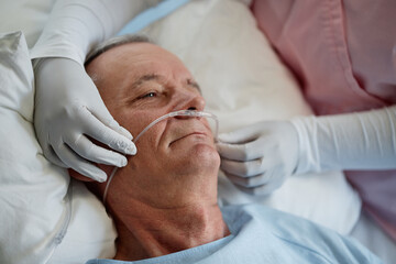 Medical professional assisting elderly male patient with oxygen nasal cannula in a hospital bed...