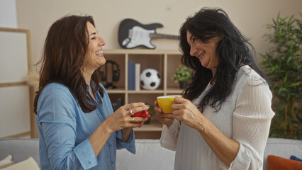 Women smiling while enjoying coffee together in a cozy living room, showcasing friendship and happiness.