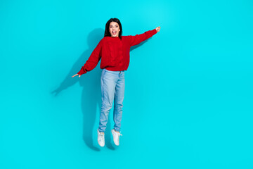 Happy young woman enthusiastically jumping with arms outstretched wearing casual fashion against...