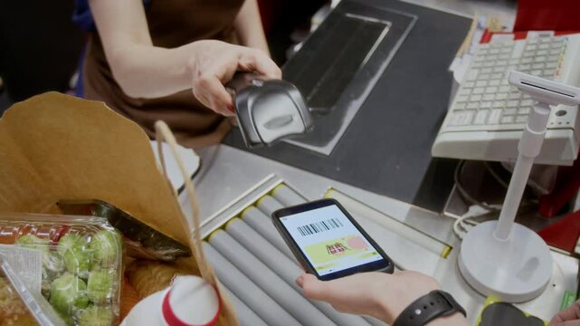 Closeup shot of unrecognizable female cashier scanning discount bar code on smartphone screen, customer buying groceries in supermarket