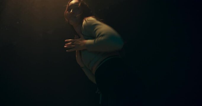 A dancer, caught in a moment of movement, enveloped by deep shadows and delicate light. The smoke adds a cinematic, dreamlike quality.