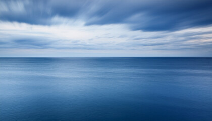 Obraz premium Tranquil Minimalist Seascape Background Created Using Long Exposure Photography, Showcasing Silky Smooth Blue Water and Ethereal Streaked Clouds - Perfect for Zen Concepts and Calming Visuals