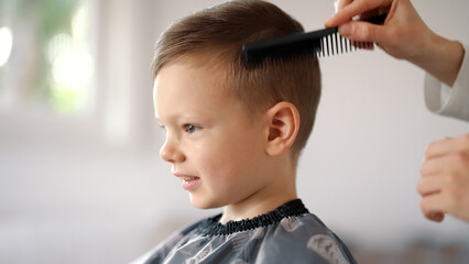 Smiling young boy getting hair cut at home. Cropped hands of young mother cutting hair of her little son. Time for a Haircut