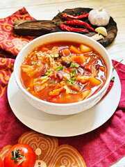 Borscht with sour cream in a white ceramic plate on a wooden background