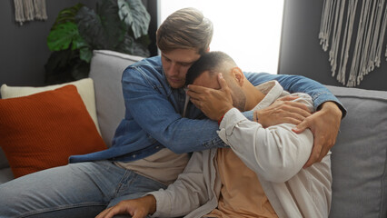 Friends comforting each other while sitting on a couch in an apartment living room.