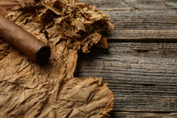 Dried tobacco leaves and cigar on wooden table, closeup. Space for text