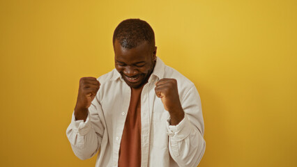 Fototapeta premium Handsome young black man standing over an isolated yellow background looking down and smiling showing fists in celebration