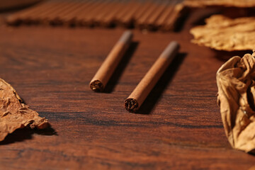 Dried tobacco leaves and cigarettes on wooden table, closeup