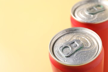 Red aluminium cans of beverage on pale yellow background, closeup. Space for text