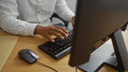 Young man working on computer indoors in an office setting, showcasing a professional workspace environment with hands on keyboard