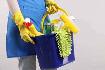 Woman with bucket of cleaning supplies on light background, closeup