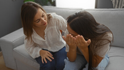 Mother comforting daughter in living room with a loving gesture, indoors at home, portraying family...