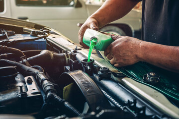 Male professional mechanic pouring antifreeze coolant liquid into car engine radiator in service...