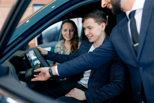 Young caucasian couple exploring new car options at dealership with male sales agent
