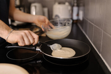 A close-up shot of a man pouring pancake batter mix into a hot frying pan