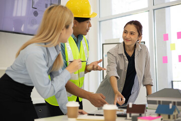 Three people are standing in a room, one of them wearing a yellow safety vest. They are looking at...