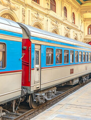 Obraz premium Vintage train carriage with blue and beige paint scheme sits on tracks beside an ornate classical-style building.